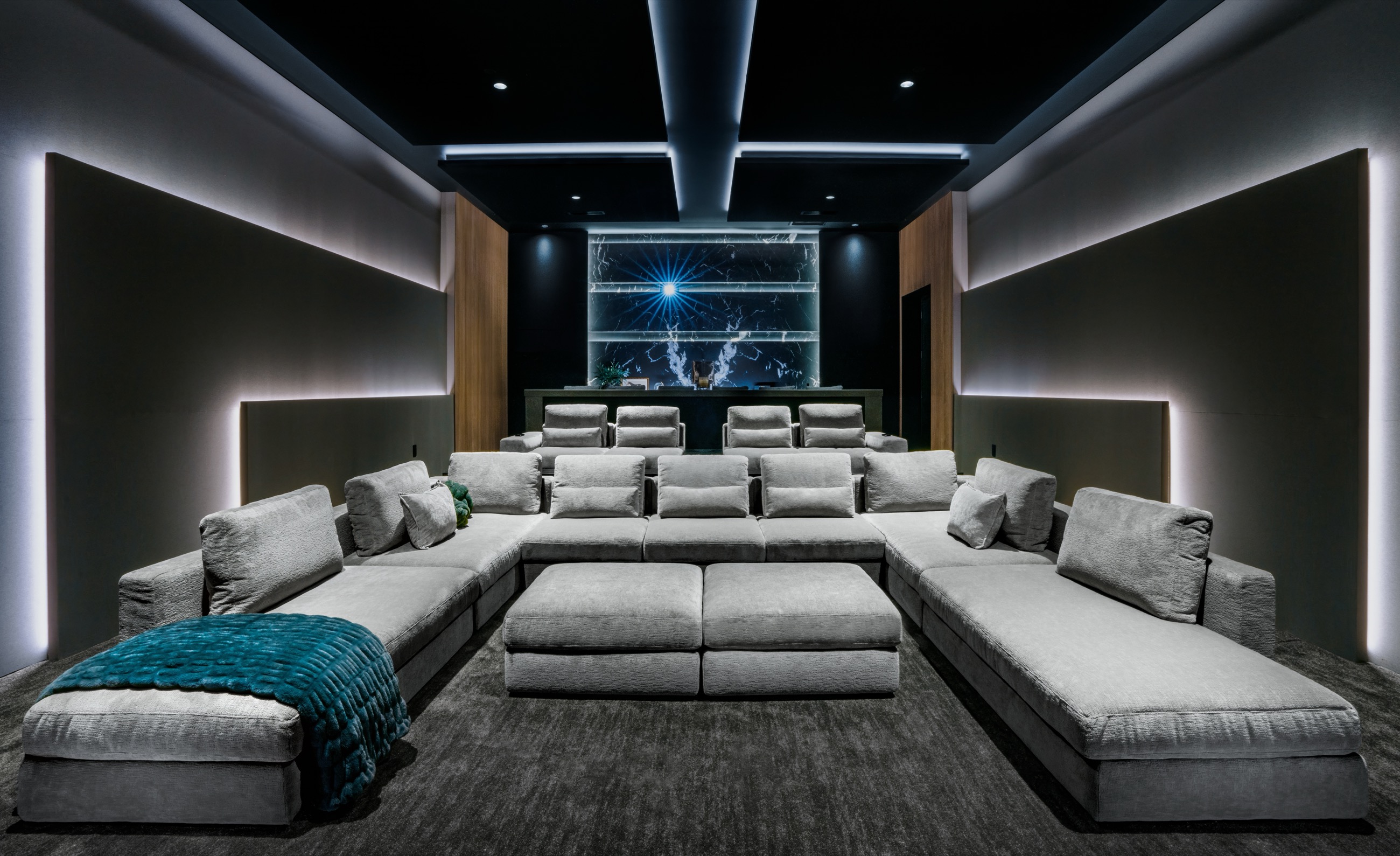 A private theater at rest, tiered seating and a lit screen wall