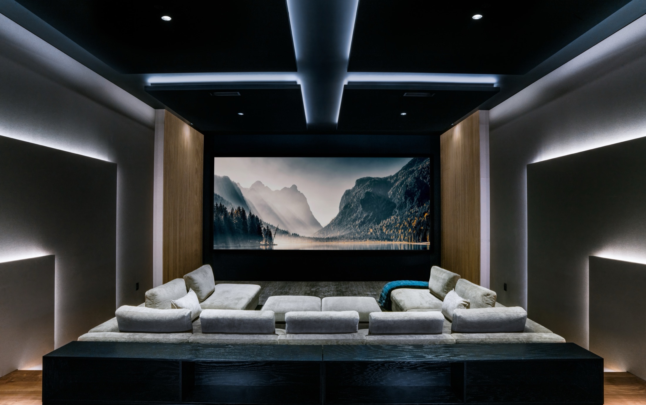 The theater at rest, screen lit, tiered seating and cove-lit acoustic walls