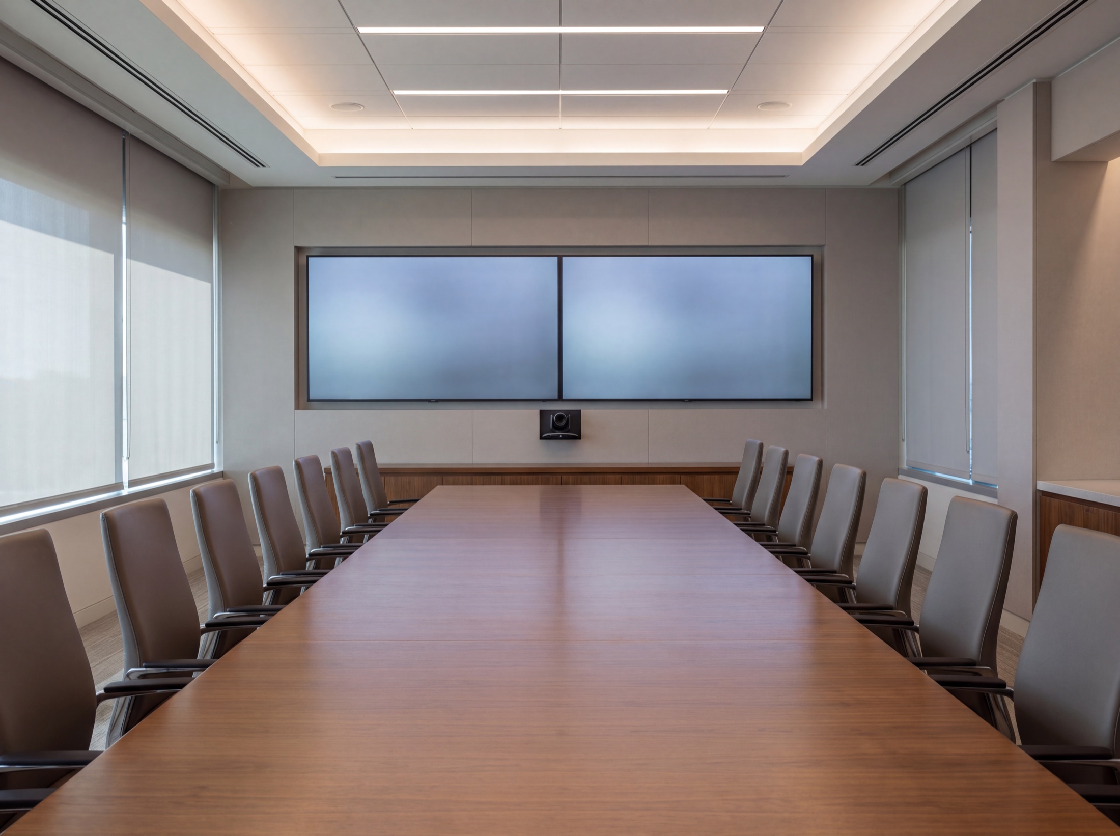 A conference room in its ready state before anyone arrives: displays awake, chairs aligned, shades at one height