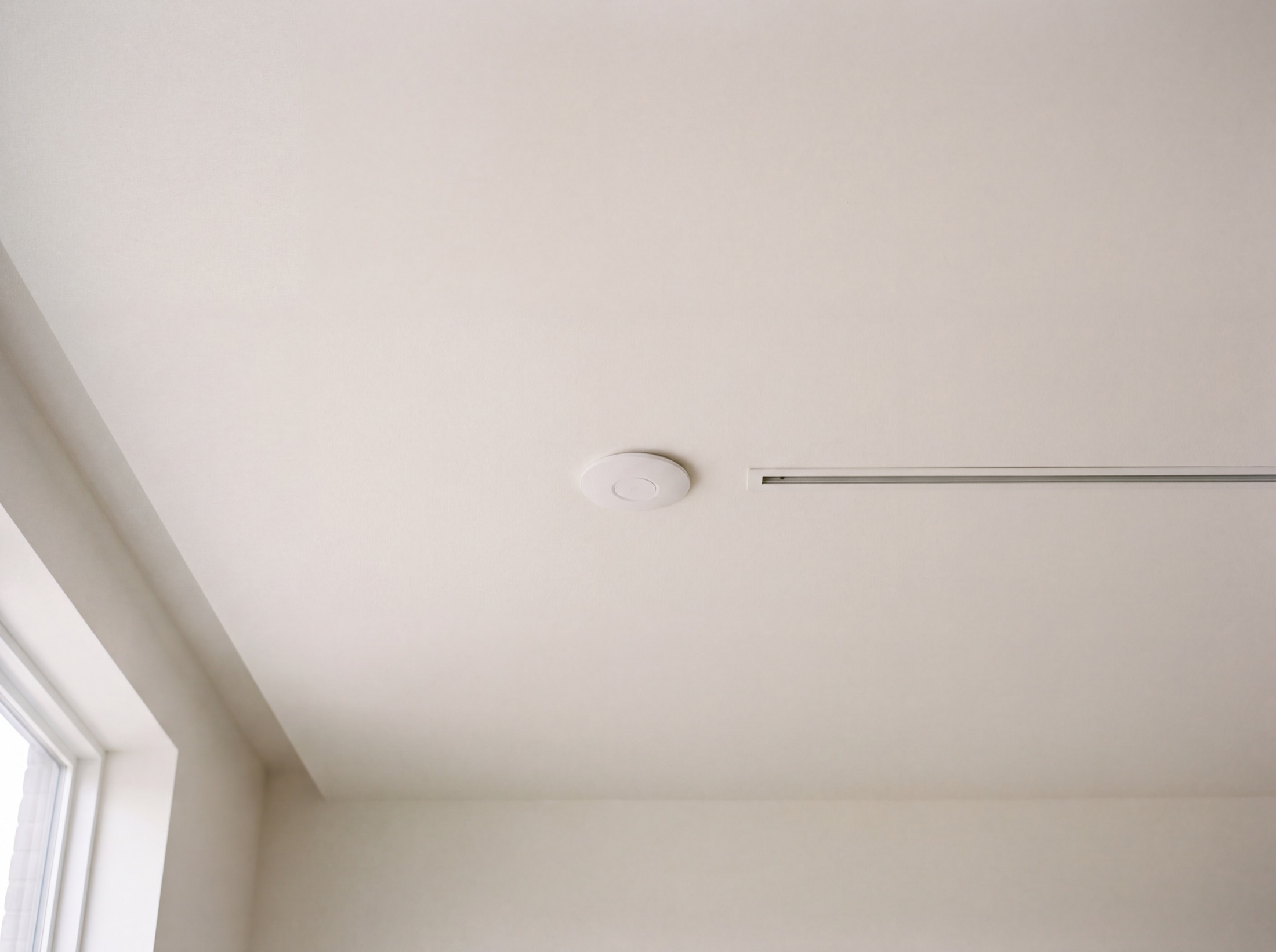 A low-profile access point sitting flush and paint-matched on a smooth ceiling plane, nearly invisible