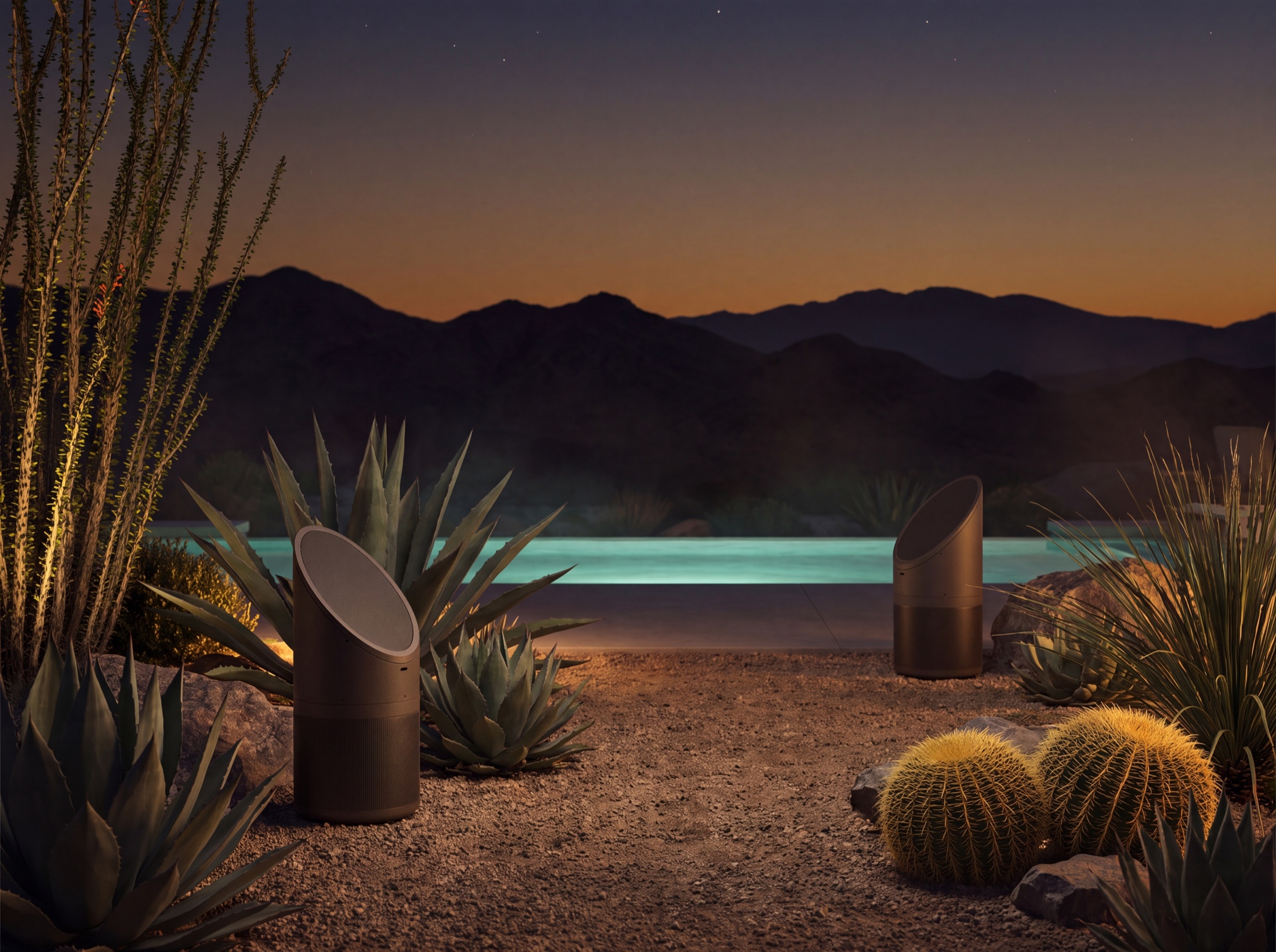 Coastal Source bollard speakers among agaves at dusk, the pool glowing beyond, mountains under an amber sky