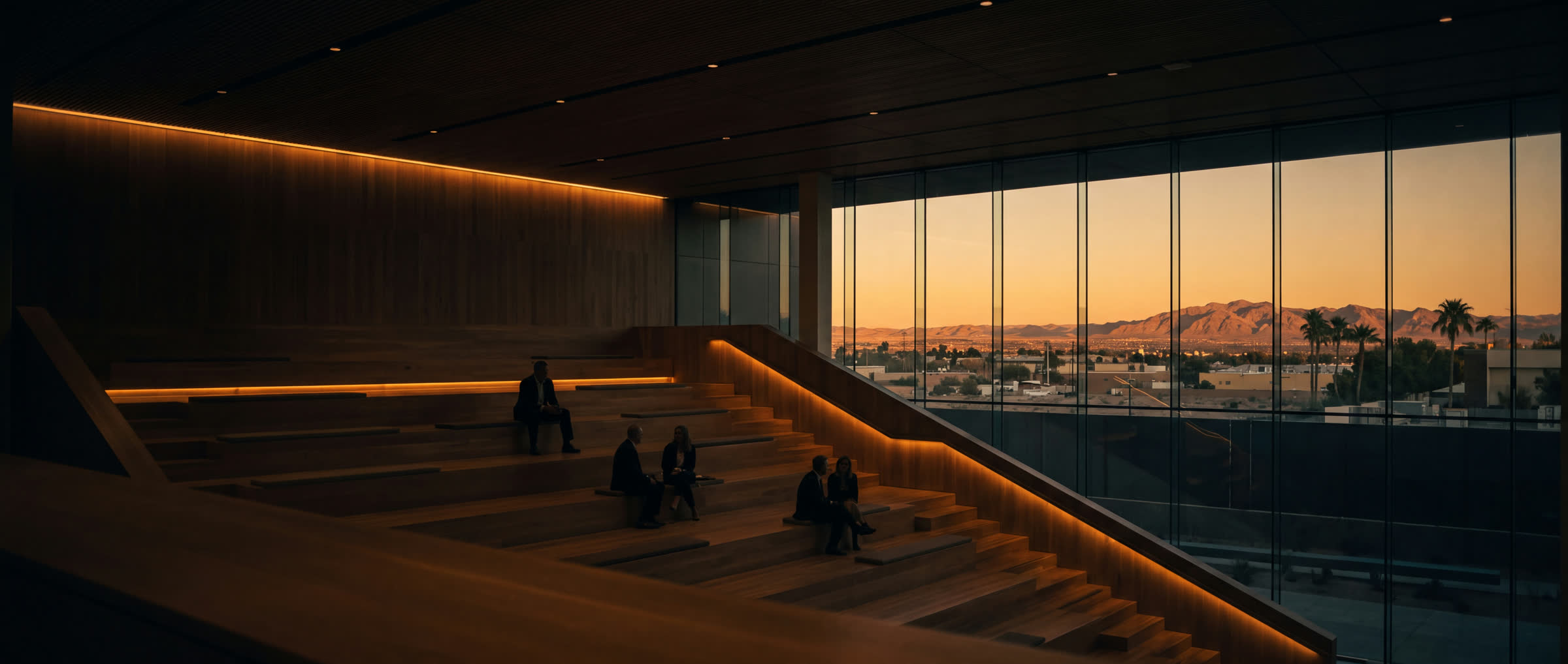 A tiered town hall at sunset, cove light tracing the seating steps, colleagues in conversation against the desert view