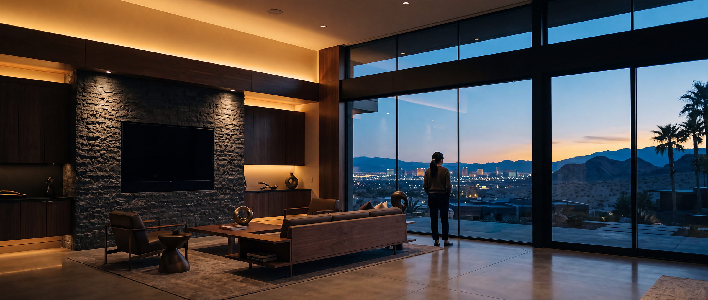 A great room at desert dusk, the Las Vegas valley beyond the glass, a resident at the window