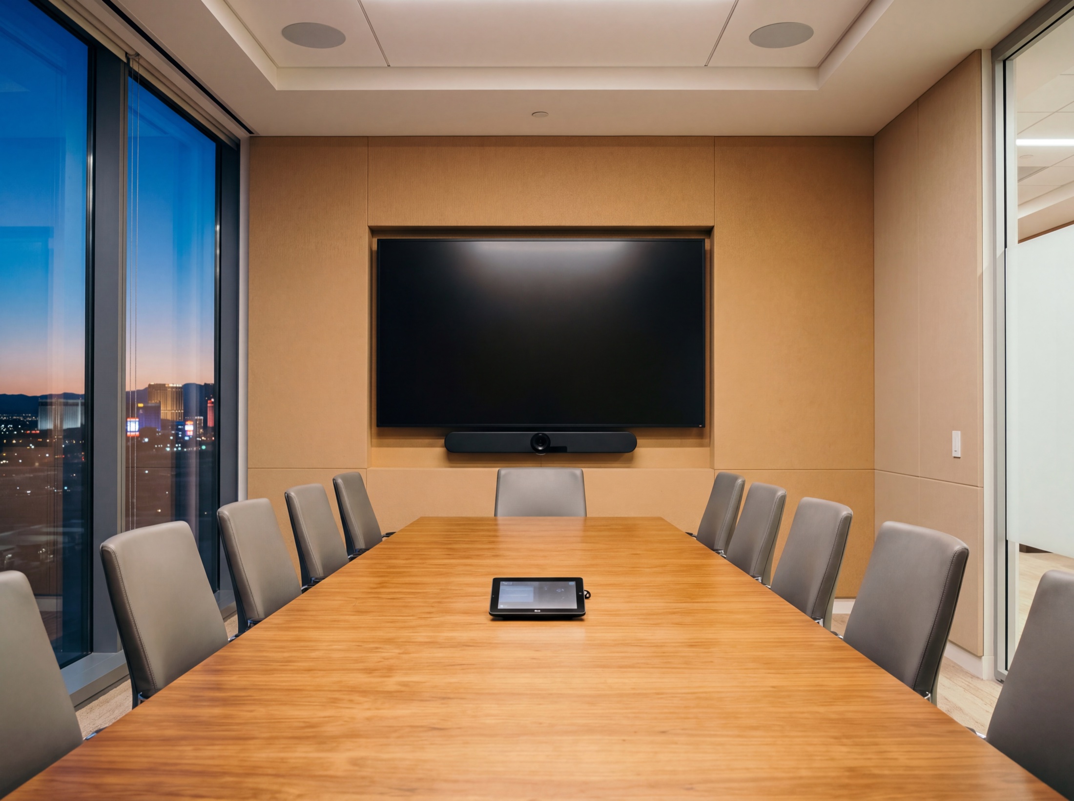 Hybrid meeting room at dusk: display and camera bar centered on the far wall, touch panel on the table, the Strip beyond the glass