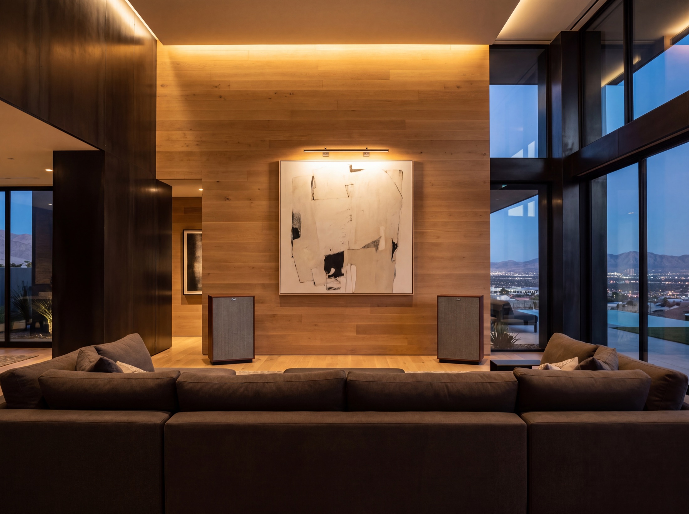 Statement loudspeakers set symmetrically against an oak wall beneath lit artwork, the Las Vegas valley beyond the glass at dusk