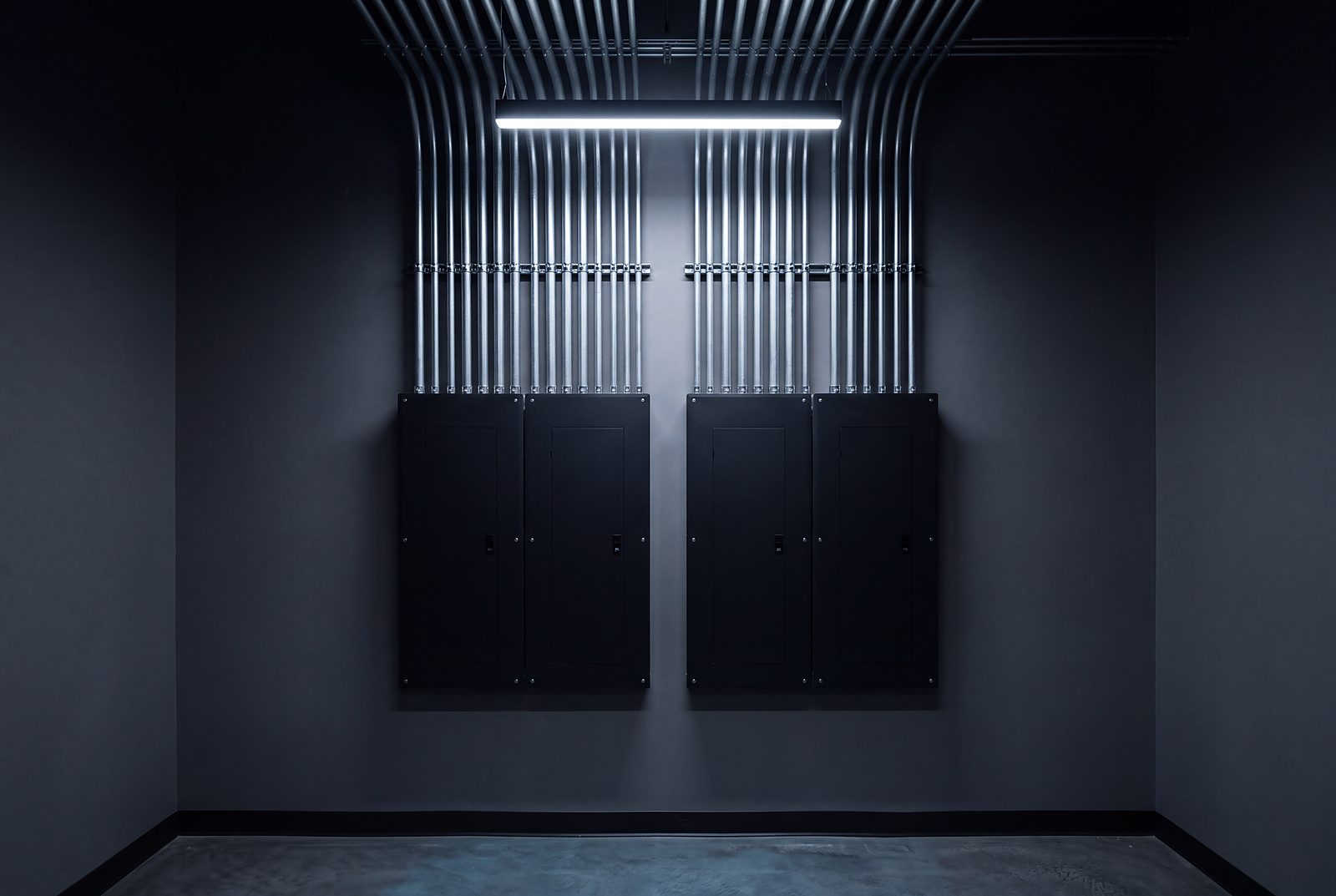 Matte black electrical panels with parallel conduit under a cool fixture