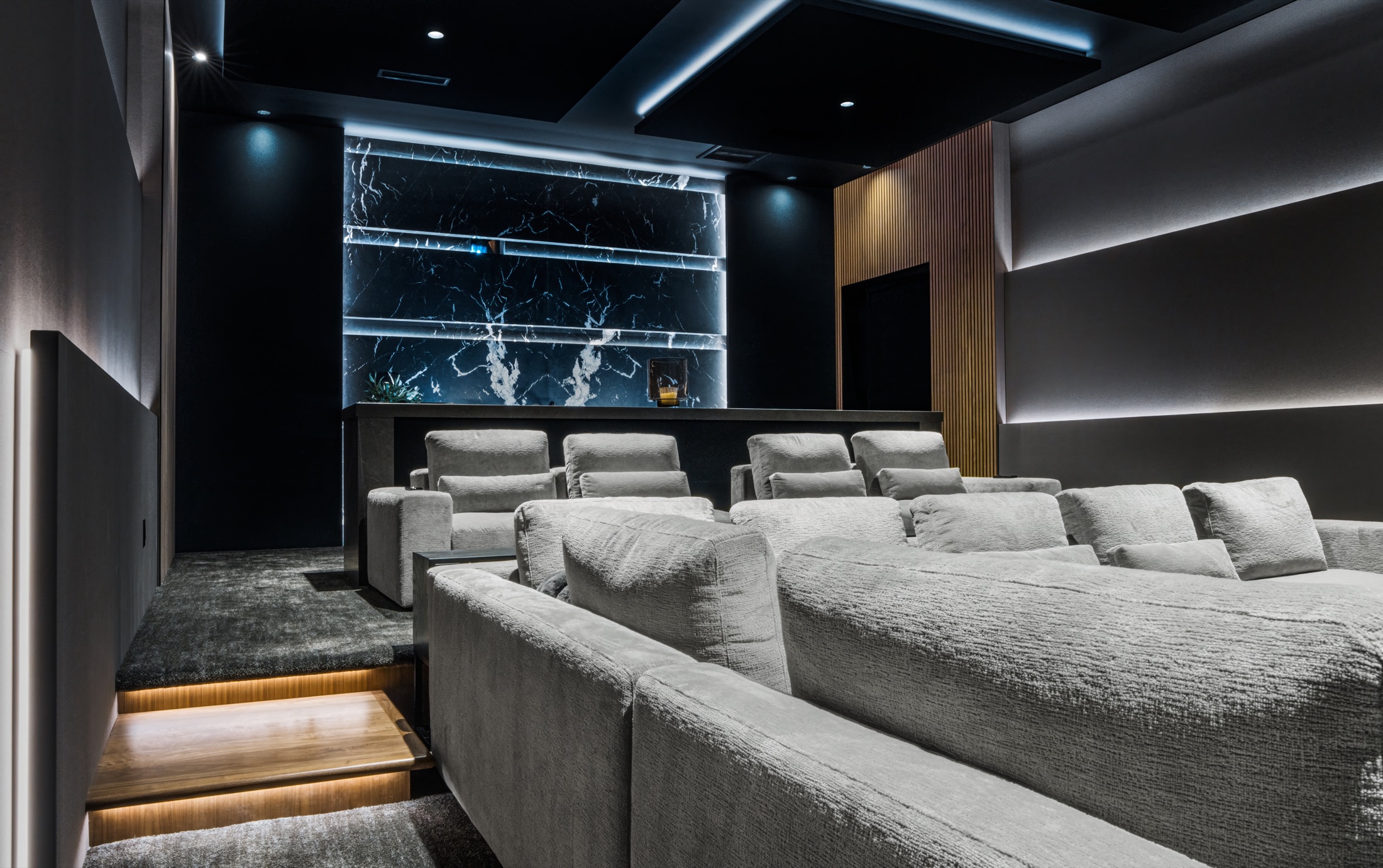 Theater seating rows under low step lighting, backlit marble bar wall behind