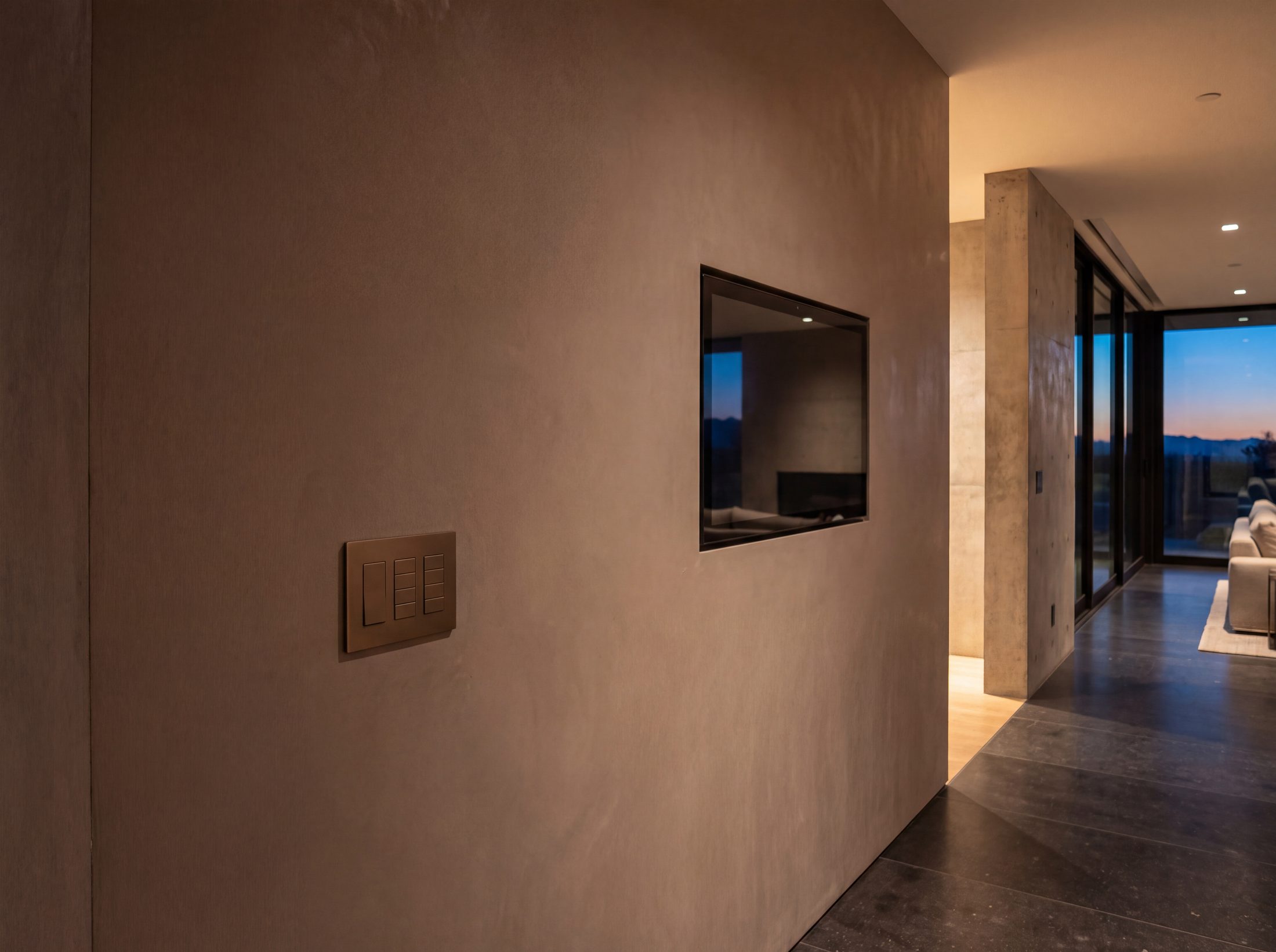 A flush keypad with blank unengraved buttons set into smooth plaster at a room entry, the house warm beyond