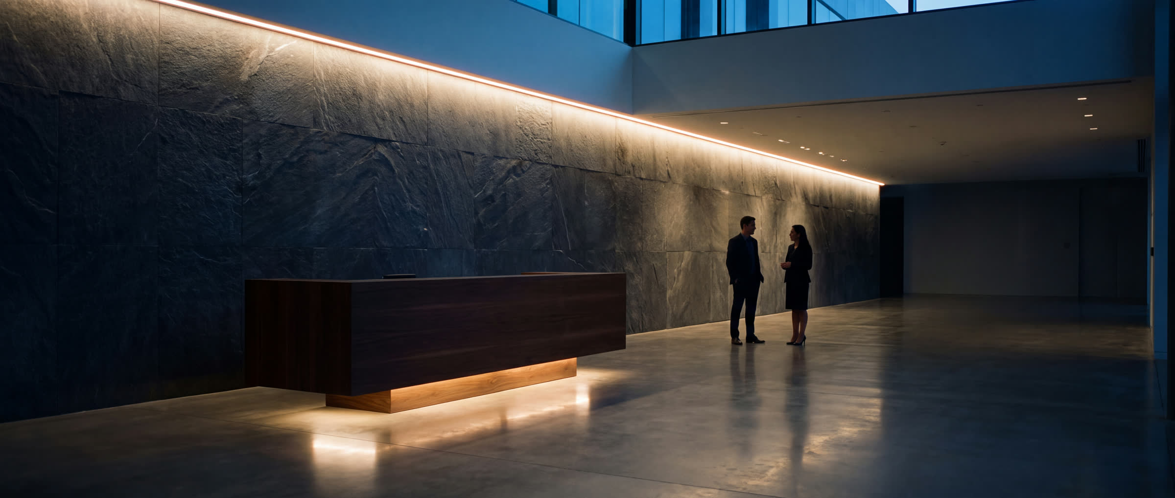 A commercial reception at dusk, two people in conversation at the cove-lit stone wall