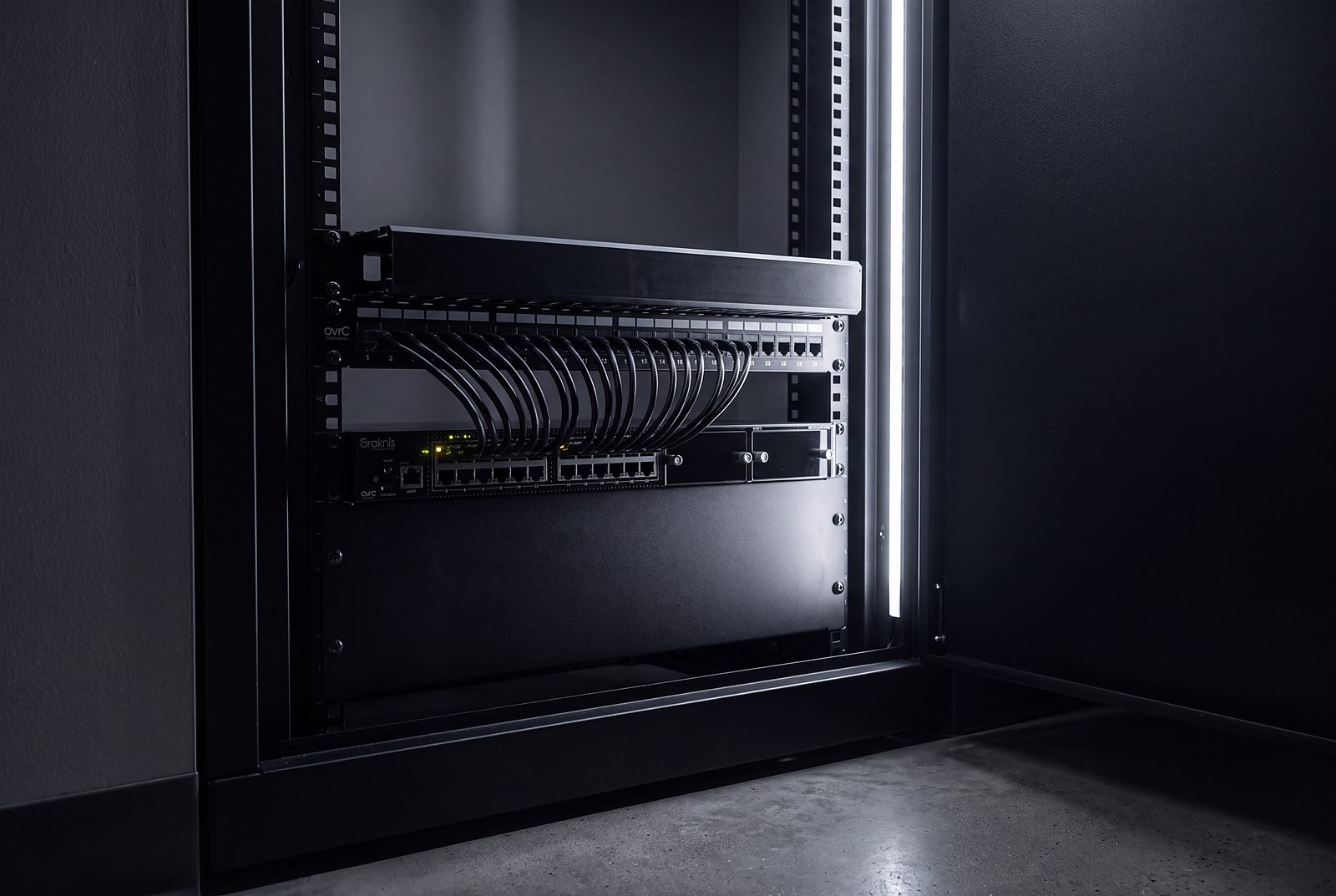 A wall-mounted network rack with combed patch leads under a cool strip light