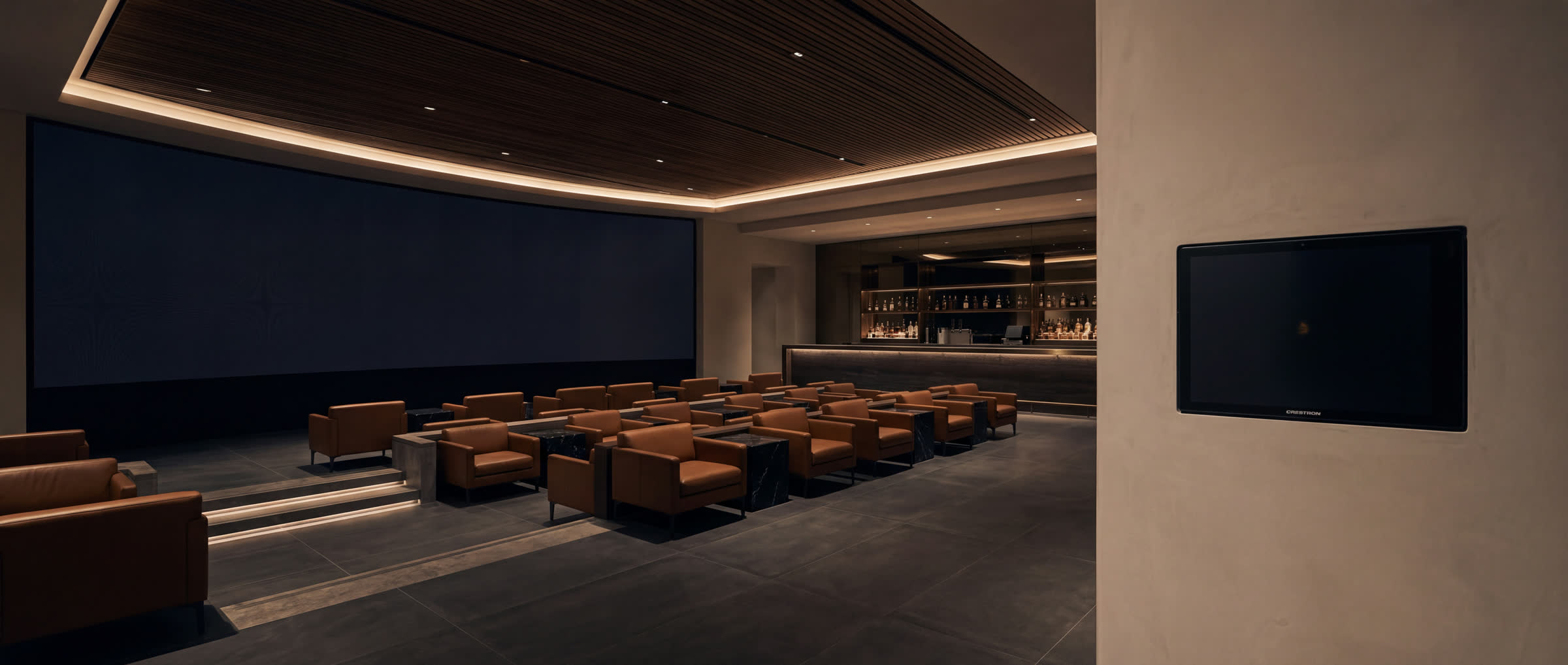 A private screening lounge in leather and walnut, bar lit behind, one control panel flush on the wall