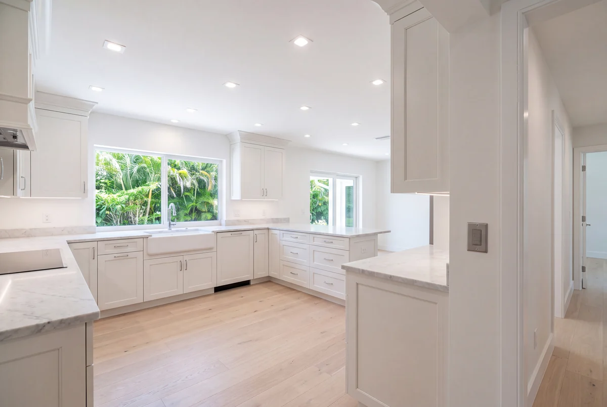 A renovated kitchen in soft white with marble counters and an even grid of recessed downlights, unlit in daylight
