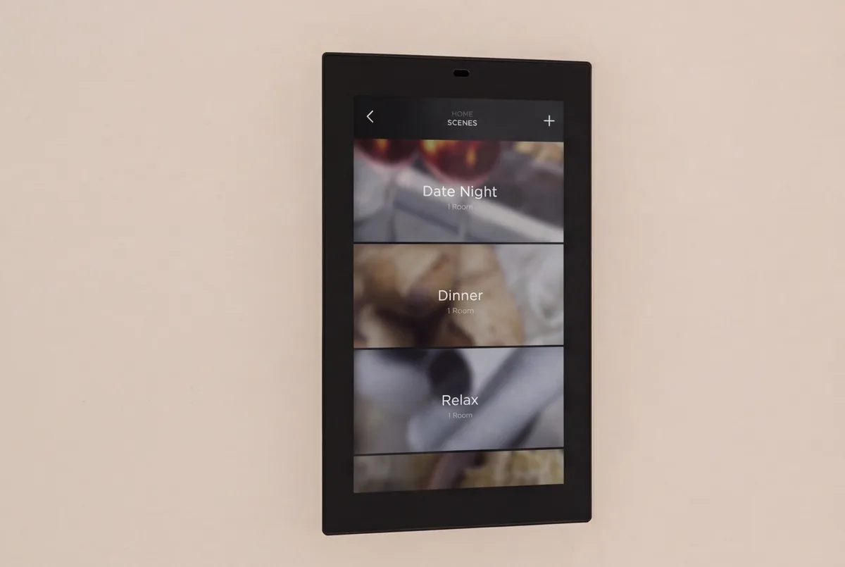 A Savant touch screen on a plaster wall showing the scenes page with Date Night, Dinner and Relax