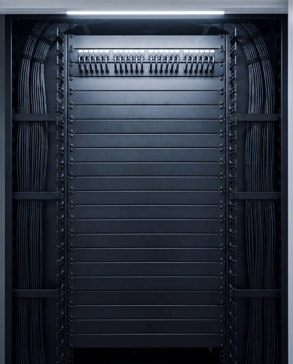 A dressed equipment rack, patch panels at the top and cable managed down both sides, lit from above