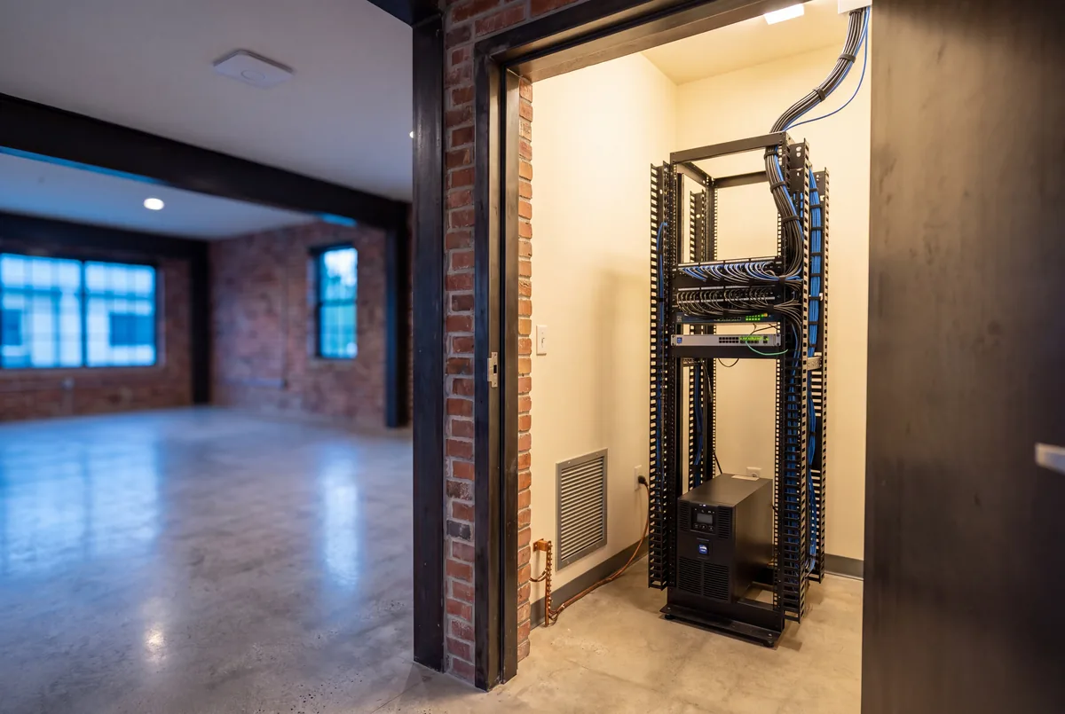A conditioned equipment closet seen through its door, with a floor standing rack, patch panel and combed cabling