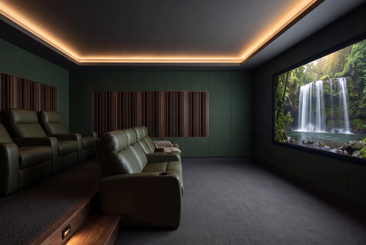 A home cinema seen from the side wall, with green felt walls, bronze slatted diffusers on the back wall and olive leather seats on risers facing the screen